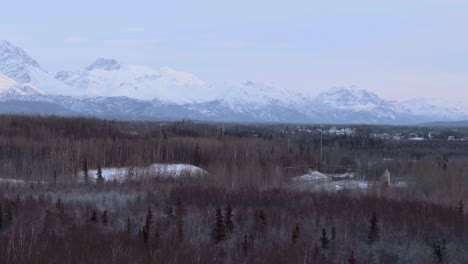 Anchorage,-pan-over-forest-in-winter-with-snow-capped-mountains-in-Alaska