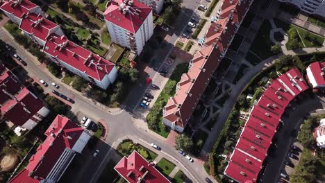 Aerial-top-down-view-flying-over-city-showing-neighborhood-houses-with-red-roofs-also-parked-cars-and-then-flying-over-road-crossing-towards-more-homes-4k