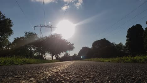 Low-shot-of-paved-biking-trail-with-the-sun-in-the-background-and-trees-with-power-lines-overhead