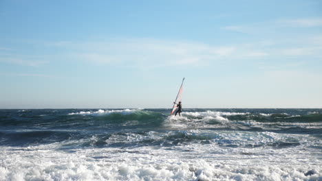 Pan-shot-of-a-norwegian-windsurfer,-surfing-a-wave,-at-the-coast-of-the-North-sea,-in-the-atlantic-ocean,-on-a-sunny,-summer-day,-in-Lista,-South-Norway