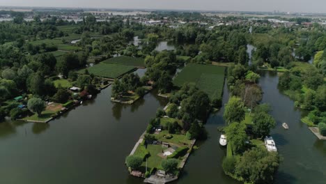 Aerial-Slomo-of-Dutch-Countryside-surrounded-with-Small-Rivers,-Green-Trees-and-Bushes,-revealing-Small-Town-in-background