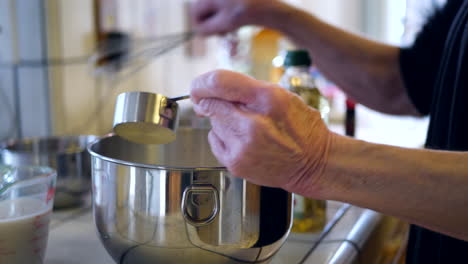 Hands-of-an-elderly-woman-chef-measuring-and-mixing-ingredients-in-a-bowl-while-baking-a-vegan-chocolate-cake-dessert-recipe