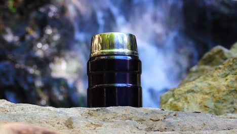 Travel-flask-at-the-waterfall,-advertising-footage-for-travellers