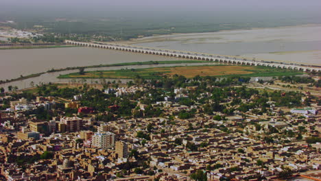 Aerial-view-of-river-and-city-with-electric-towers-in-river,-Two-big-canals-starting-from-the-river-going-between-the-city,-Rural-and-urban-areas-gathered-Khyberpakhtunkhwa,-Pakistan