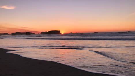 Bunter-Sonnenuntergang-An-Der-Küste-Von-Oregon-In-Bandon-Mit-Felsnadeln-Im-Hintergrund-Und-Wellen,-Die-Kommen-Und-Gehen