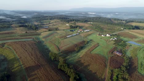 Aerial-camera-view-of-West-Virginia-countryside-with-farms,-fields,-mountains-and-fog-settling-in-the-valleys