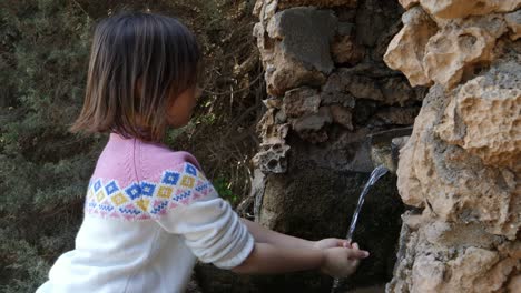 Mittlere-Ansicht-Eines-Süßen-Kleinen-Mädchens,-Das-Sich-In-Einer-Natürlichen-Quelle-Die-Hände-Wäscht