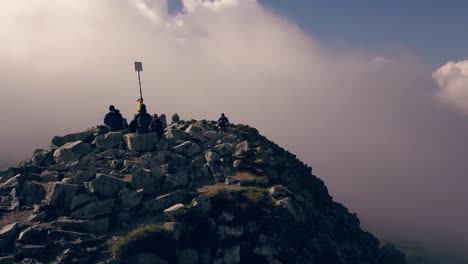 Wide-drone-shot-rotating-around-hikers-sitting-at-top-of-a-mountain