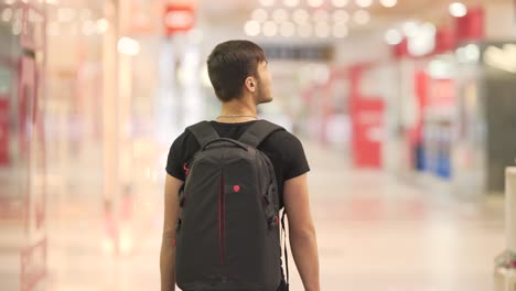 Young-guy-with-a-black-backpack-walking-in-the-mall-and-looking-through-the-shops
