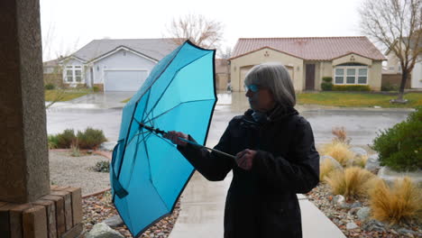 A-pretty-middle-aged-woman-walking-in-out-of-the-winter-rain-and-putting-away-her-blue-umbrella-in-a-neighborhood-SLOW-MOTION