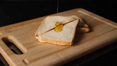 Honig-Fließt-In-Zeitlupe-Auf-Zwei-Gerösteten-Broten-Auf-Einem-Schneidebrett