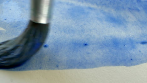 Artist-paints-blue-with-paint-brush-and-water-colors-on-white-paper