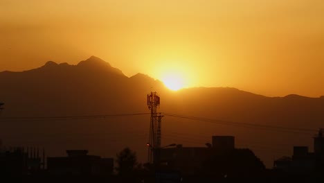Sunset-at-the-mountains-near-a-city,-silhoutte-view-with-a-sattelite-tower,-houses-and-buildings,-low-angle
