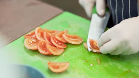 Close-up-of-a-cook's-hands-with-white-latex-gloves,-cutting-red-juicy-tomatoes-with-a-professional-knife,-on-a-green-plastic-cutting-board