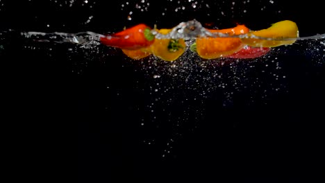 Colorful-sweet-peppers-being-dropped-into-water-in-slow-motion