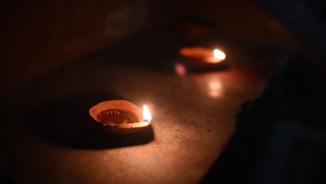 Two-lighted-Diyas-on-stairs-for-celebration-of-Diwali-or-christmas-at-night,-flames-reflecting-on-floor
