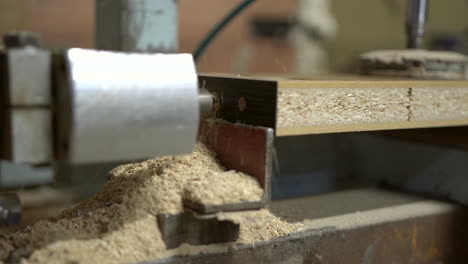 Horizontal-technical-drill-bit-goes-in-and-out-into-chipboard-wooden-element,-producing-a-lot-of-flying-sawdust-arround
