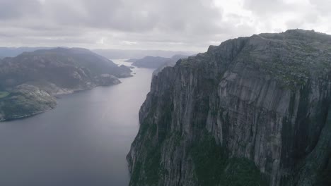 Aerial-Slomo-shot-of-Norwegian-Mountains,-revealing-Fjord-and-a-large-bridge-in-the-background,-during-Cloudy-weather