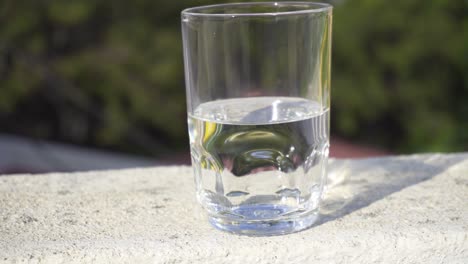 Glass-half-filled-with-water-isolated-against-an-out-of-focus-background,-slow-zoom