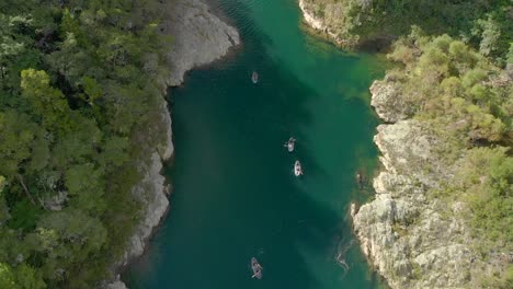 People-on-kayak-trip-paddle-boats-through-canyon-on-Pelorus-river,-New-Zealand-with-native-forrest-and-rock-boulders--Aerial-Drone