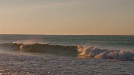 Small-waves-breaking-during-a-calm-sunrise-in-Luz,-Portugal