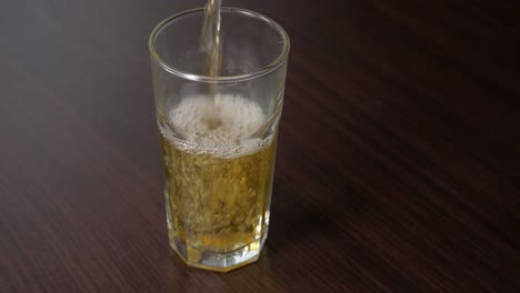 Pouring-apple-juice-into-tall-glass-on-a-wooden-table
