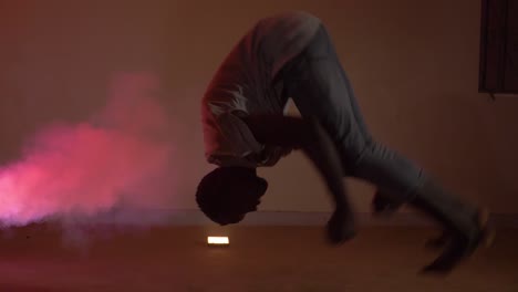 Slow-motion-shot-of-African-youth-doing-a-back-flip-from-a-crouching-position-in-colorful-smoke