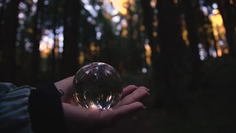 close-up-of-a-young-female-hand-holding-a-crystal-ball-reflecting-landscape-in-an-autumnal-forest