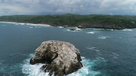 Aerial-shot-of-a-big-rock-formation-and-the-coastline-of-Zipolite,-Oaxaca