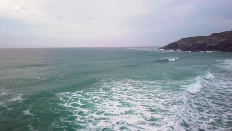 Surfer-swimming-through-choppy-waves-alongside-headland.-Drone-shot