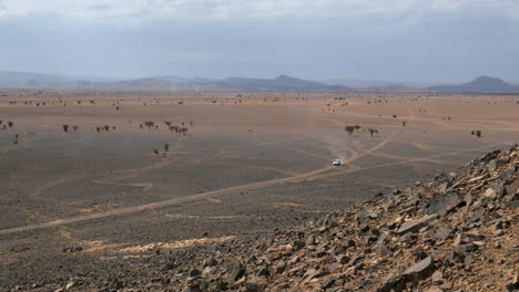 Pickup-truck-driving-through-an-hot-desert-vally-in-the-Sahara,-Morocco