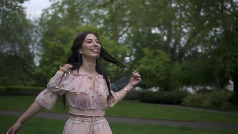 Attractive-and-carefree-brunette-tourist-spinning-around-with-a-floral-dress-at-the-park-in-London,-happy-and-cheerful