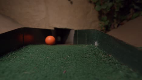 An-orange-mini-golf-ball-going-into-the-last-section-of-the-course