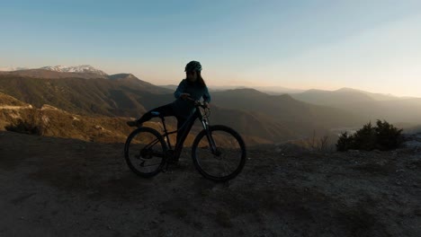Girl-riding-her-bike-and-stopping-on-a-mountain-at-sunset