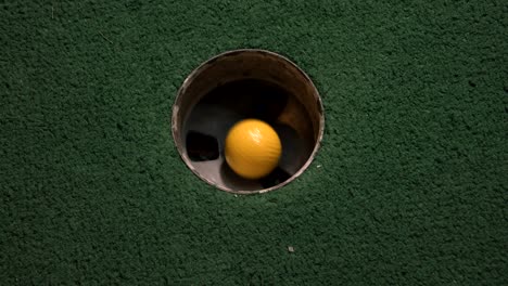 Eine-Nahaufnahme-Eines-Gelben-Minigolfballs-Aus-Der-Vogelperspektive,-Der-In-Das-Golfloch-Fällt-Und-In-Der-Tasche-Auf-Einem-Platz-Abprallt