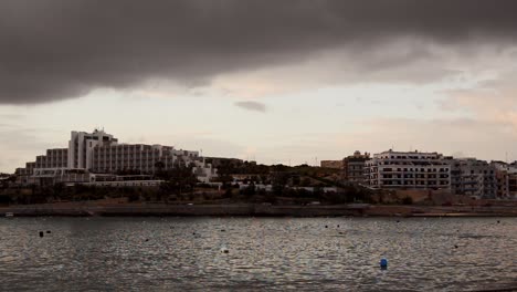 early-morning-in-Qawra,-Malta,-before-sunrise,-rainy-stormy-clouds-over-buildings-and-early-morning-traffic