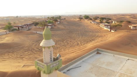 Aerial-view-of-an-empty-abandoned-village-and-homes-with-a-mosque-covered-in-desert-sand-near-Dubai
