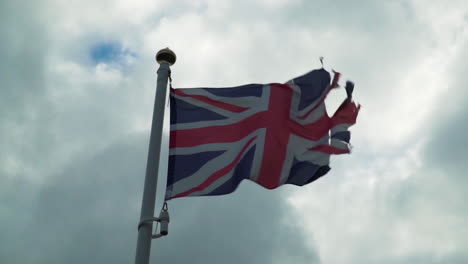Old-Union-Jack-Flag-Blowing-in-Strong-Wind-Against-Clouds-in-Slow-Motion