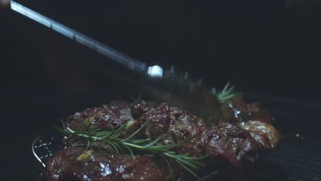 Two-sets-of-tongs-shuffle-around-rosemary-and-press-garlic-cloves-into-Butterflied-Lamb-Cuts-on-the-BBQ