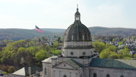 Aerial-drone-view-of-the-Cathedral-of-the-Blessed-Sacrament-in-Altoona,-Pennsylvania-with-the-American-flag-seen-behind