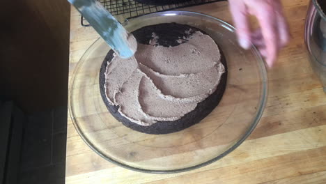 Man's-hands-seen-frosting-a-chocolate-cake-in-a-home-kitchen