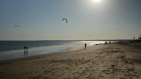 Zwei-Kitesurfer-Und-Einige-Leute-Bei-Sonnenuntergang-Am-Strand