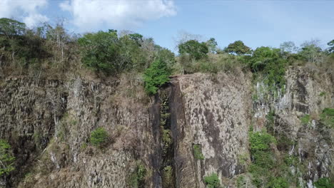 Aerial-shot-flying-towards-the-crest-of-a-dried-out-waterfall-in-Meseta-de-Chorcha,-Black-vultures-flying-across,-Chiriqui,-Panama