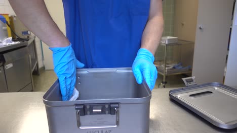 Ein-Sterilisationsspezialist-Reinigt-Einen-Instrumentenbehälter-Mit-Einem-Alkoholgetränkten-Tuch