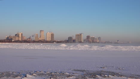 Wind-Weht-Schnee-über-Einen-Zugefrorenen-See-Mit-Einer-Skyline-Der-Stadt-Im-Hintergrund-Im-Winter-Chicago-4k