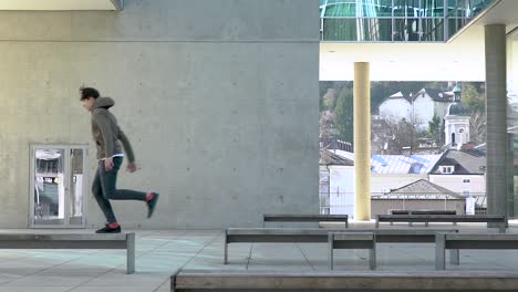 Slow-motion-shot-of-a-young-parkour-athlete-jumping-from-bench-to-bench-in-a-urban-place