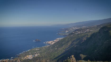 Scenic-green-hillside-slopes-toward-azure-sea-far-below-and-small-coastal-town-of-Tenerife,-Canary-Islands