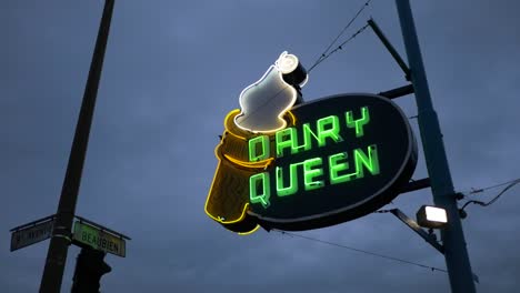 Dairy-Queen-retro-neon-sign-glowing-below-a-dark-cloudy-evening-sky-in-Montreal