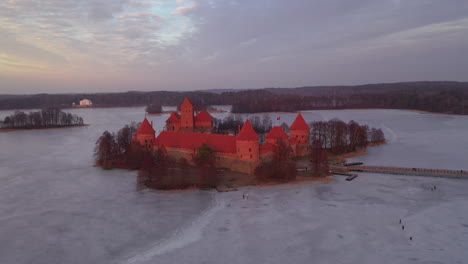 AERIAL:-Rotating-Shot-of-Trakai-Island-Castle-With-Bridge-Path-Over-Frozen-Lake-with-People-Skating-on-Ice