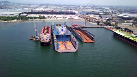 Aerial-view-of-logistics-concept-a-cargo-ship-being-retrofit,-repair-and-services-on-a-floating-dry-dock-off-the-coast-at-Laem-Chabang-dockyard-in-Chonburi-Province,-Thailand